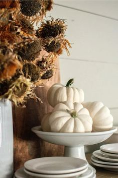 white pumpkins and dried flowers in a bowl on a table with plates around them