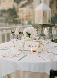 the table is set with white plates and silverware, candles and flowers in vases