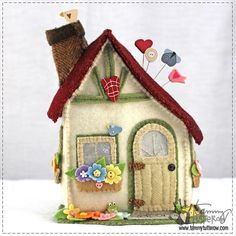 a small white house with red roof and flowers on the front door is sitting on a table