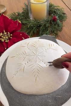 someone is carving a snowflake on a white plate with red flowers in the background