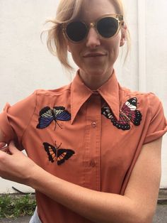 a woman in an orange shirt with butterfly appliques on her collar and sleeves