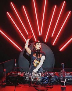 a woman standing in front of a dj set with red lights on the wall behind her