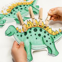 a child's hand is holding clothes pins and placing them on a dinosaur cutout