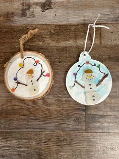 two snowman ornaments hanging from string on wood