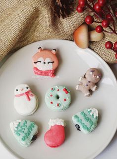 small decorated cookies on a white plate next to red berries and an acorn tree