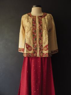 "I'm not sure, but I think the outfit is made of dupion silk. The top/jacket/kameez is heavily embroidered on the front and cuffs with metallic thread (Zardozi embroidery), beads and sequins. It's flared at the bottom, has side slits and hook-and-eye closure up the front. The voluminous skirt/salwar has a sheen to it and has gold thread dot pattern woven into it, with a metallic gold trim on the hem. It has a drawstring waist with a side zipper. The saree/dupatta is made from the same fabric. Bo Bollywood Style Designer Chanderi Nehru Jacket, Chanderi Long Sleeve Sharara For Festive Occasions, Long Sleeve Chanderi Sharara For Festive Occasions, Traditional Front Open Choli With Dupatta, Traditional Front Open Sharara With Dupatta, Navratri Chanderi Nehru Jacket With Resham Embroidery, Navratri Chanderi Nehru Jacket With Cutdana, Traditional Front Open Sharara With Zari Work, Long Sleeve Art Silk Anarkali Set With Dori Work