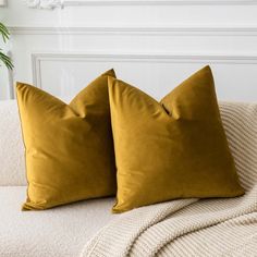 two yellow pillows sitting on top of a white couch next to a potted plant