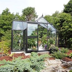 a glass house in the middle of a garden with lots of trees and plants around it