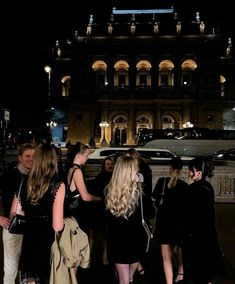 a group of people standing in front of a building at night with cars parked on the street