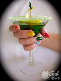 a woman's hand holding a martini glass with green and yellow nail polishes