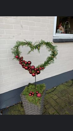 a heart - shaped decoration made out of christmas balls and greenery in front of a brick wall