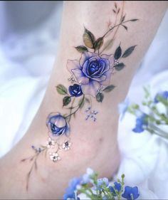 a blue rose tattoo on the ankle is shown with flowers and leaves around it,