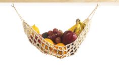 a hammock filled with assorted fruit on top of a wooden table next to a white wall