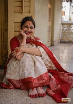 a woman sitting on the ground in a white and red sari with her hand under her chin