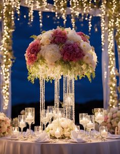 a table topped with lots of white and pink flowers next to tall vases filled with candles