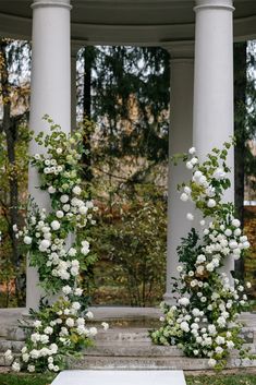 two white flowers are growing on the pillars in front of a gazebo with columns