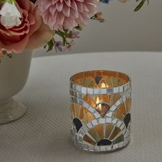 a vase filled with flowers next to a lit candle on top of a white table