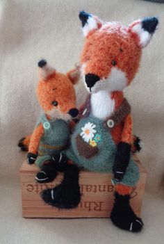 two knitted foxes sitting on top of a wooden box with the word supple tote written below them