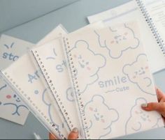 a person holding three notebooks with the words smile cute written on them and teddy bears drawn on them