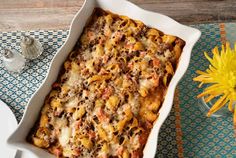 a casserole dish with cheese and meat in it on a table next to a yellow flower