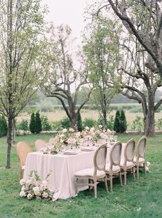 an outdoor table set up for a formal dinner in the grass with flowers and greenery