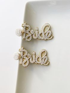 the bride and groom name brooches are on a white plate with gold beads