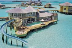 an aerial view of a beach resort with water slides and thatched huts on stilts