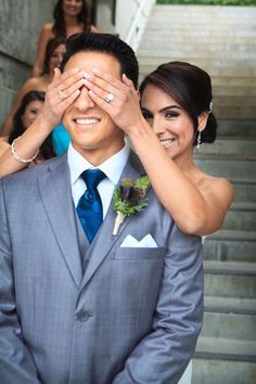 a bride and groom are covering their eyes as they stand on the steps outside with other people in the background