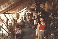 a woman standing in front of a market with lots of items hanging from it's ceiling