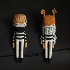 two crocheted stuffed animals wearing sweaters and hats, sitting on a black surface