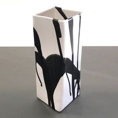 a black and white square vase sitting on top of a gray table next to a wall