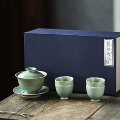 three tea cups and saucers in front of a boxed box on a wooden table