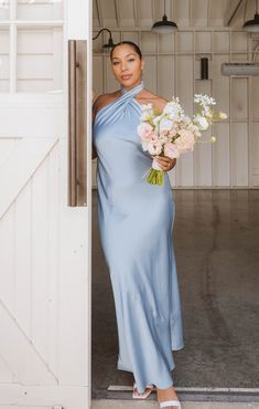 a woman in a blue dress is holding flowers and posing for the camera with an open barn door behind her