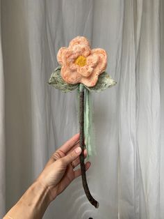 a hand holding a fake flower on top of a wooden stick in front of a white curtain