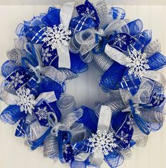 a blue and white christmas wreath hanging on a door with snowflakes, bells and ribbons