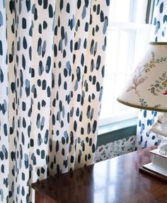 a lamp on a table next to a window with blue and white curtains in front of it