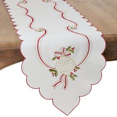 a white table runner with red trim and holly decorations on the edge is sitting on a wooden bench