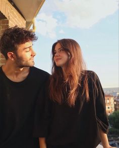 a man and woman standing next to each other on top of a roof looking at the sky