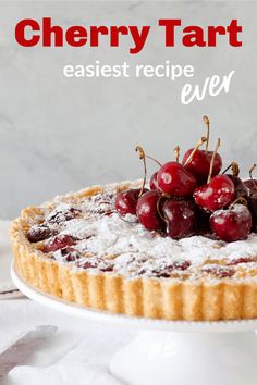 a cherry tart with powdered sugar and fresh cherries on top, sitting on a white cake plate