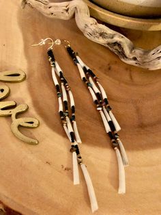 a pair of earrings sitting on top of a piece of wood next to a bowl