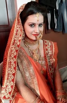 a woman dressed in an orange and gold bridal outfit with jewelry on her face