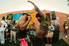 two men dancing on the grass in front of a brick wall with people standing around