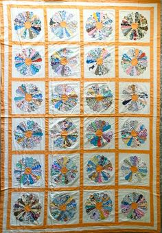 an orange and white quilt is hanging on the side of a wall with flowers in it