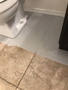 a white toilet sitting in a bathroom next to a wooden cabinet and tiled flooring