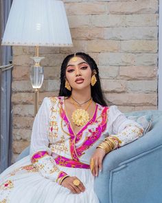 a woman sitting on top of a blue couch wearing a white dress and gold jewelry