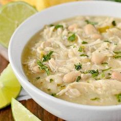 a white bowl filled with chicken chili and garnished with cilantro next to lime wedges