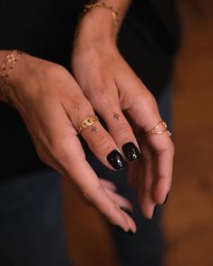 a woman's hands with black and gold nail polish holding onto her ring finger