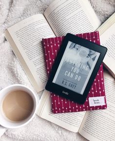 an open book sitting on top of a bed next to a cup of coffee and two books