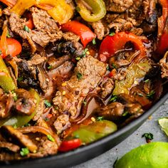 a skillet filled with meat, peppers and limes on top of a table