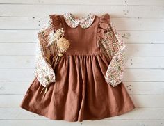 "This beautiful pinafore dress is made of soft medium weight prewashed linen. It has the pinafore style, closes at the back with coconut wood buttons. It has shoulder frill, does not tighten at the waist and has a maximum length at the knee. Perfect outfit for autumn!  Pay attention to the sizes for a good fit. SIZE GUIDE: 12-18 months: height 33.1\", chest 20.9\", waist 20.5\" 18-24 month: height 36.2\", chest 22\", waist 21.3\" 2-3 years: height 39.4\", chest 22.8\", waist 21.7\"   3-4 years: Spring Dress-up Brown Dress, Brown Spring Dress For Dress-up Occasions, Brown Dress For Spring Dress-up Occasion, Casual Cotton Suspender Dress With Ruffles, Cottagecore Brown Dress For Spring, Brown Ruffled Dress For Garden Party, Spring Brown Pinafore Dress, Spring Cotton Pinafore Dress For Garden Party, Cotton Cottagecore Pinafore Dress